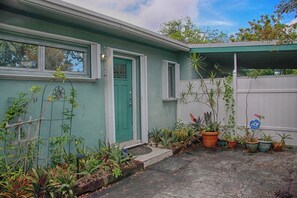 Ein Haus mit grüner Tür, einer überdachten Veranda und diversen Blumentöpfen.