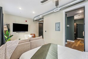 Et moderne hotelværelse med en seng, en sofa, et fjernsyn og en synlig dør til et badeværelse.