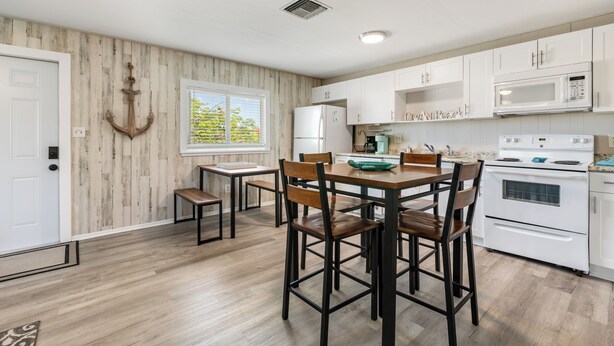 A kitchen with white cabinets, a wooden dining table, and a large window. - Peaceful 2-bedroom house with CABANA CLUB in charming Key Colony Beach (Duck Key)
