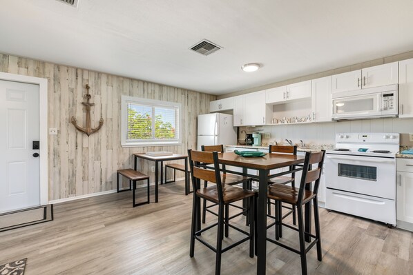 A kitchen with white cabinets, a wooden dining table, and a large window. - Peaceful 2-bedroom house with CABANA CLUB in charming Key Colony Beach (Duck Key)