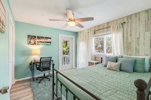 A bedroom with a bed, a desk, a chair, a ceiling fan, a window with curtains, and a door. - Peaceful 2-bedroom house with CABANA CLUB in charming Key Colony Beach (Duck Key)