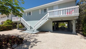 A two-story building with a white staircase leading to a balcony, a number '280' sign, and a gravel driveway. - Peaceful 2-bedroom house with CABANA CLUB in charming Key Colony Beach (Duck Key)