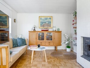 Ein Wohnzimmer mit einer Couch, einem Holzkabinett, einem runden Couchtisch, einem Kamin und einem Gemälde an der Wand.