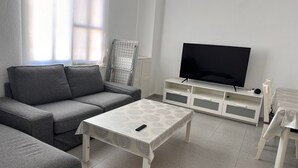 A living room with a grey sofa, a TV on a white stand, a patterned table, and a window with blinds. - Apartment for seasonal rent. Ramiro Maetzu Street pta. 7 (València)