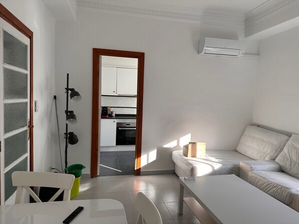 Una sala moderna con sofá, mesa de comedor y cocina visible a través de una puerta abierta.