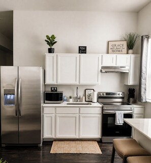 A modern kitchen with white cabinetry, stainless steel appliances, a microwave, a sink, and a countertop with a clock and a sign.