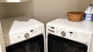 Dos lavadoras Maytag de carga frontal en un cuarto de lavado, con una cesta de mimbre y una botella de detergente sobre la encimera.