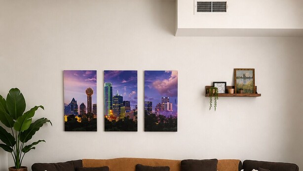 Una sala moderna con un sofá seccional marrón oscuro, una mesa de centro de madera y tres cuadros con vistas urbanas en la pared.