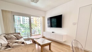 Ein modernes Wohnzimmer mit einer Couch, einem Couchtisch, einem an der Wand montierten Fernseher und einer Glastür, die auf einen Balkon führt.
