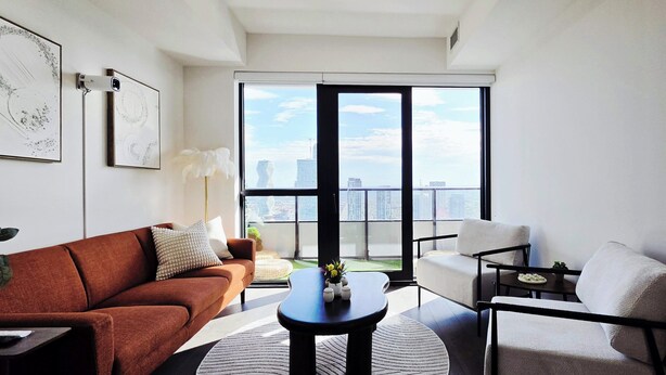 Ein modernes Wohnzimmer mit Sofa, Sessel, Couchtisch und Blick auf die Stadt durch große Fenster.