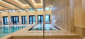 Une piscine intérieure dotée d’une zone peu profonde signalée par la mention « ZONE PEU PROFONDE 1,1 M » et de plusieurs portes donnant accès à d’autres espaces.
