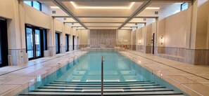 A long indoor swimming pool with clear water, surrounded by walls with a light wood finish and modern lighting fixtures. - Sky High | Luxe Stay | 2 BR-2 BA | SQ1 | Lake View | Gym | Pool | Parking (Mississauga)
