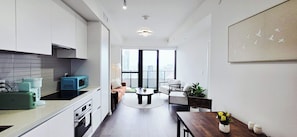 Une cuisine moderne dotée d’appareils électroménagers intégrés, un coin repas avec une table ronde et une grande fenêtre offrant une vue sur la ville.