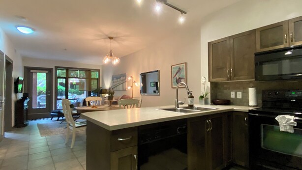 A modern kitchen with dark cabinetry, a central island, and a dining area with chairs and a table. - Resort-Style Stay in the Heart of Kelowna’s Lower Mission (Kelowna)