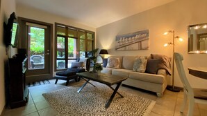 A living room with a sofa, a coffee table, a TV, and a large window. - Resort-Style Stay in the Heart of Kelowna’s Lower Mission (Kelowna)