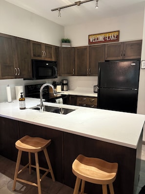 Una cocina moderna con armarios de madera oscura, un refrigerador negro, una encimera de mármol blanco y un letrero que dice 'Welcome to the Lake'.