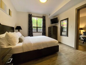 A bedroom with a bed, a TV, a dresser, and a window with curtains.