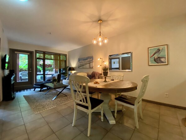 A dining area with a round table, white chairs, a chandelier, and a painting on the wall.