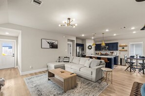 Un salon moderne avec un canapé d’angle, une table basse et un coin repas agrémenté d’un lustre.