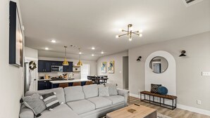 Ein modernes Wohnzimmer mit grauem Sofa, Couchtisch aus Holz und einer Küche im Hintergrund.