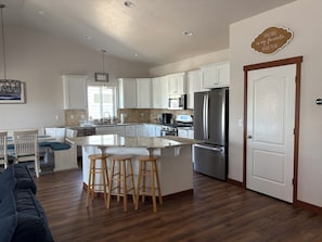 A modern kitchen with white cabinets, a stainless steel refrigerator, and a wooden island with stools. - Prairie Falls  Oasis (Post Falls)