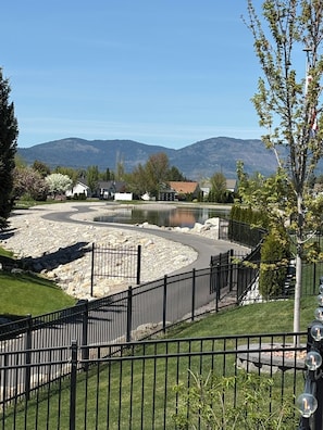 A landscaped area with a curved pathway, a body of water, and a mountain backdrop. - Prairie Falls  Oasis (Post Falls)