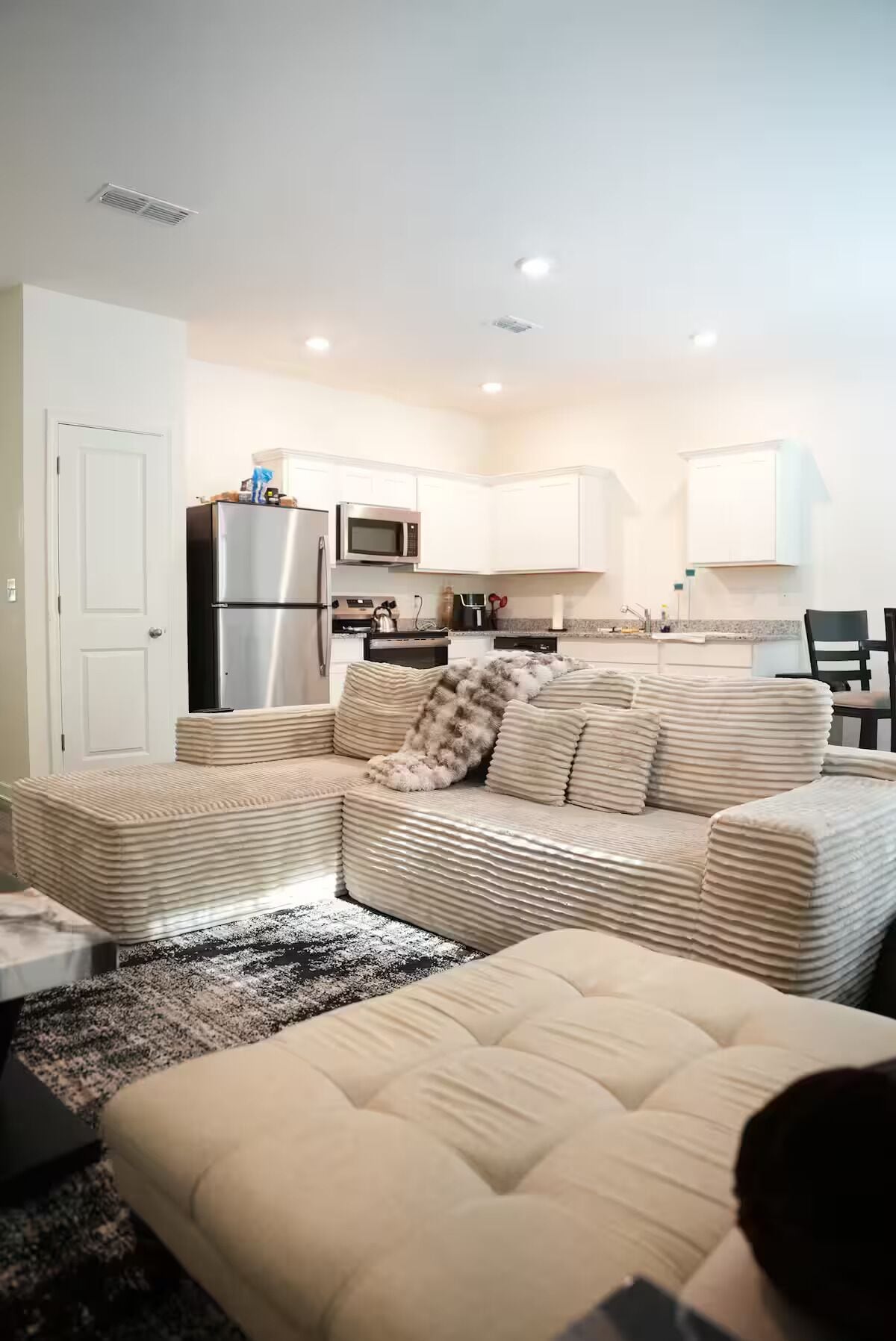 A modern living room with a sofa, a coffee table, and a kitchen area in the background.