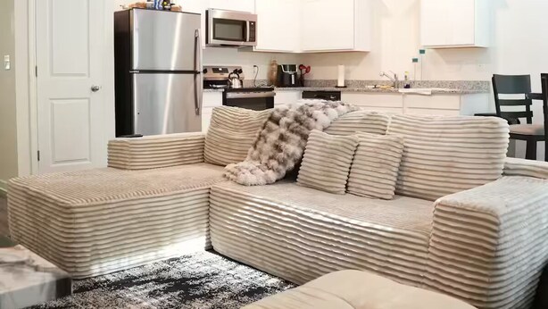 En moderne stue med sofa, sofabord og et køkken i baggrunden.