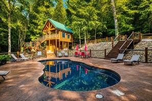Eine Holzhütte mit Pool, umgeben von Bäumen und einer Steinmauer.