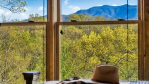 Una habitación con un ventanal que ofrece vistas a un bosque y montañas.