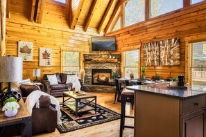 Ein Holzblockhaus-Interieur mit Kamin, Holzwänden, einer Couch, einem Couchtisch und einem Essbereich.