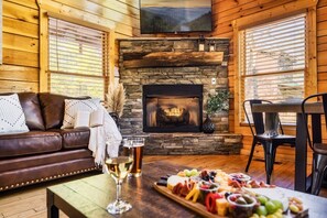 Ein gemütliches Blockhaus-Interieur mit Kamin aus Stein, Ledersofa und einer Wurst- und Käseplatte.