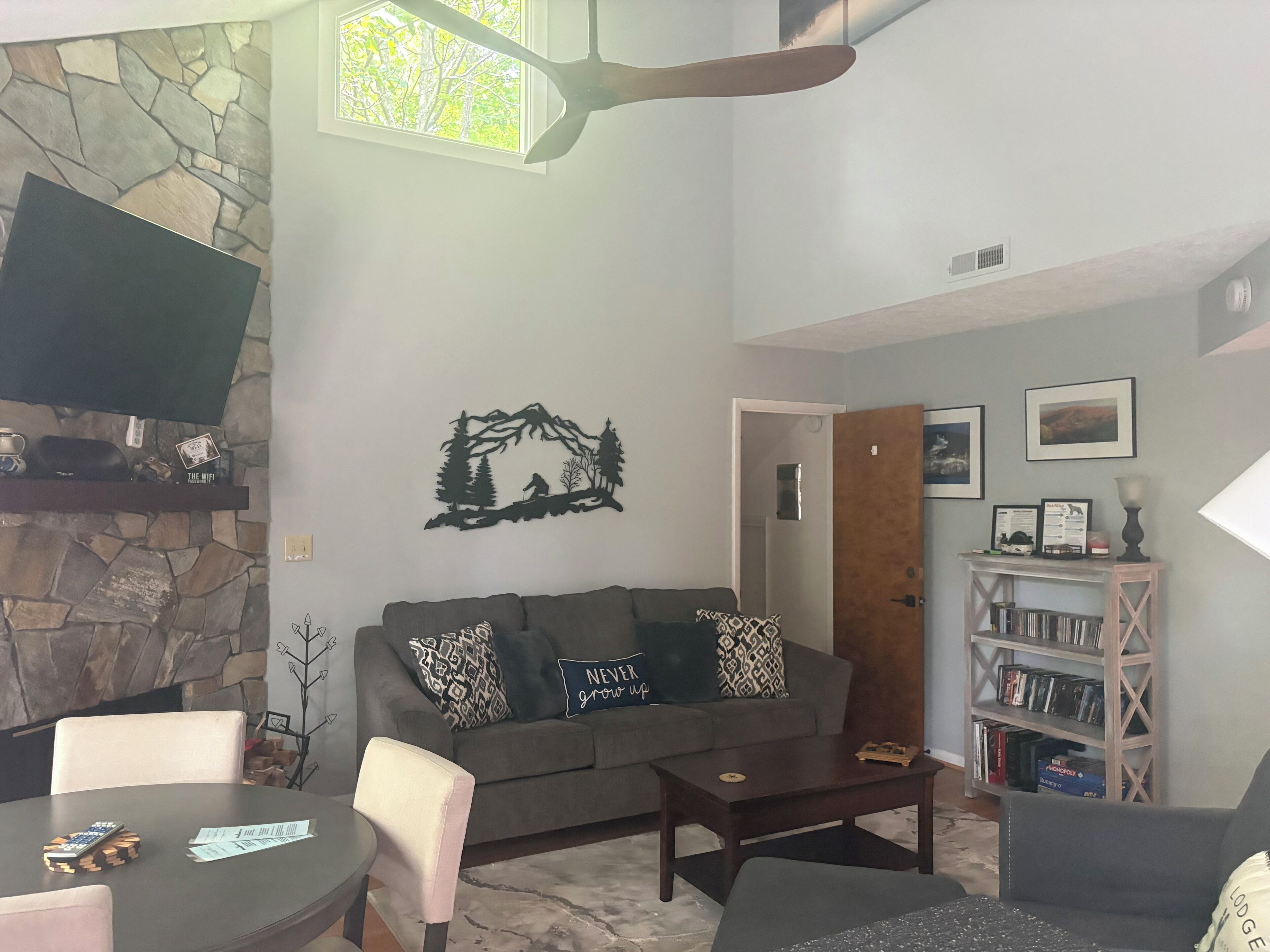 A living room with a stone wall, a mounted TV, a sofa with patterned cushions, a coffee table, and a bookshelf.