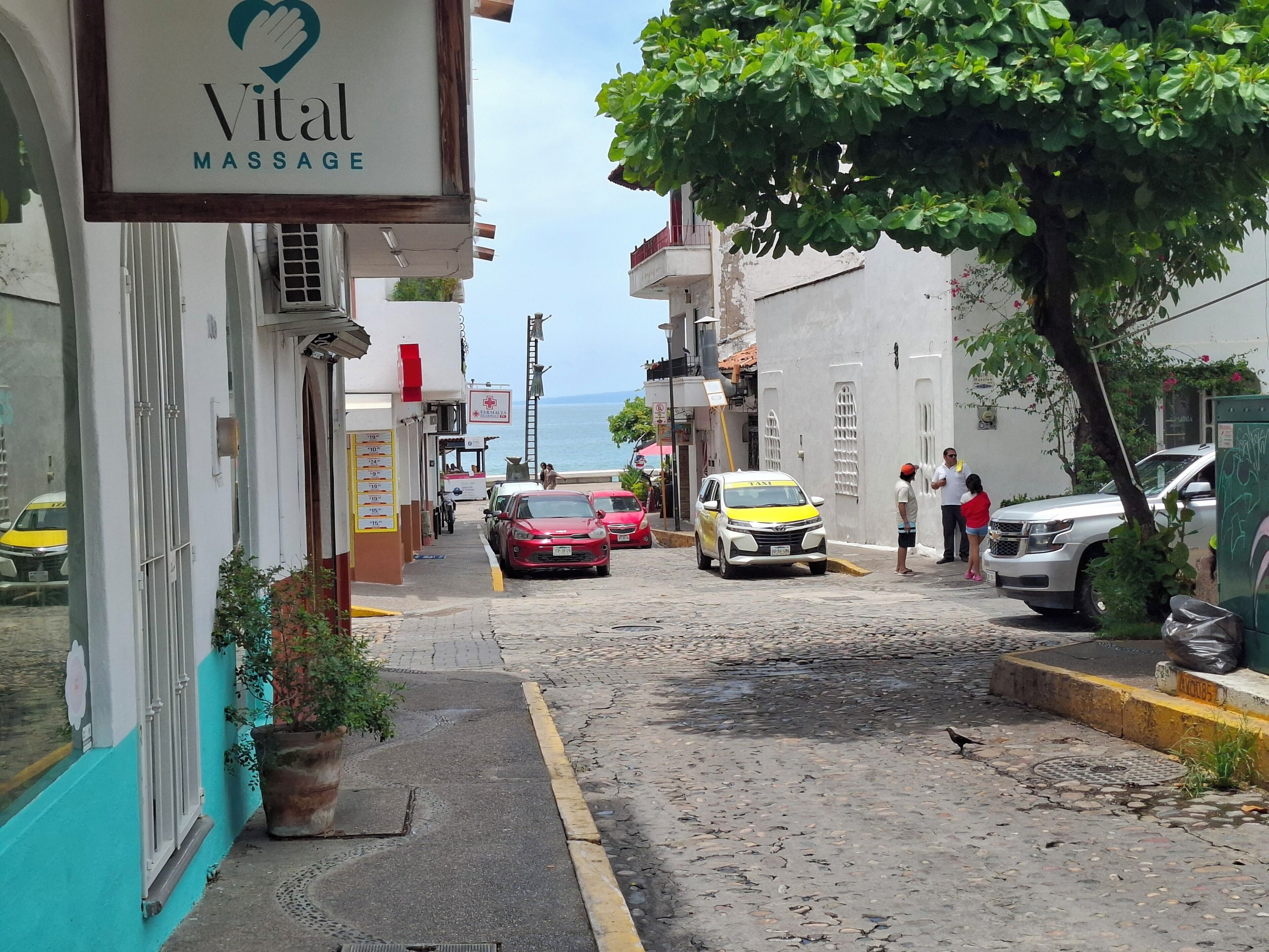 Una calle con una clínica de masajes, autos estacionados y un árbol.