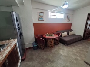 Ein gemütlicher Wohnraum mit Küchenzeile, einem Essbereich mit Tisch und Stühlen, einer Couch und einem Deckenventilator.