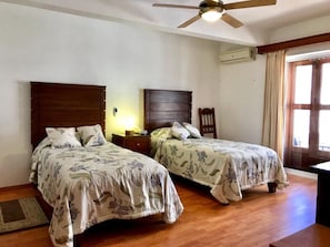 Ein Schlafzimmer mit zwei Betten, einem Deckenventilator, einer Klimaanlage und einem Fenster mit Vorhängen.