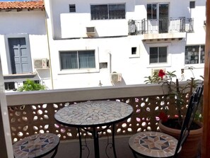 Ein Balkon mit rundem Tisch und zwei Stühlen, einem Blumentopf und einem Gebäude mit Balkonen im Hintergrund.