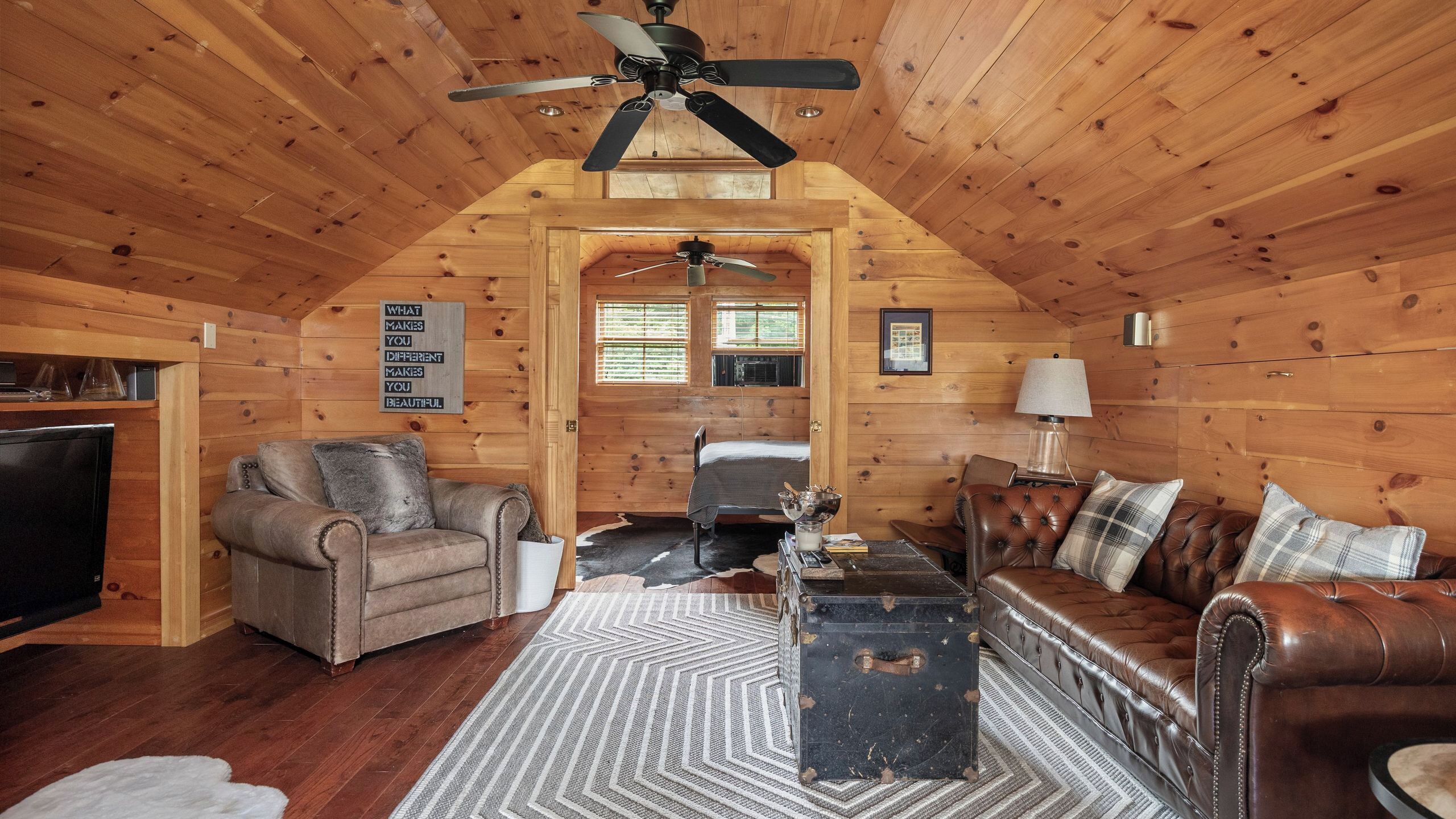 A log cabin interior with a ceiling fan, a television, a fireplace, a sofa, and a dining table.