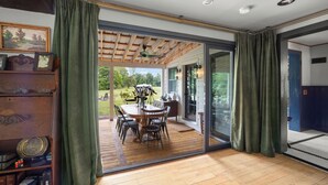A room with a wooden floor, a dining table with chairs, a bookshelf, and a sliding glass door leading to an outdoor area with a patio and a view of the outdoors. - Farmhouse at Leeds by Avantstay Walled Garden + Soaking Tub + Private Barn Near Hudson (Leeds)