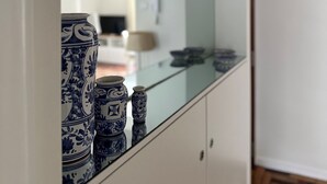 Een keuken met een glanzende achterwand, witte kasten en blauwe, patroonrijke vazen op het aanrecht.