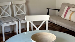 Een kamer met een ronde tafel, twee witte stoelen, een bank en vier foto's in lijsten aan de muur.