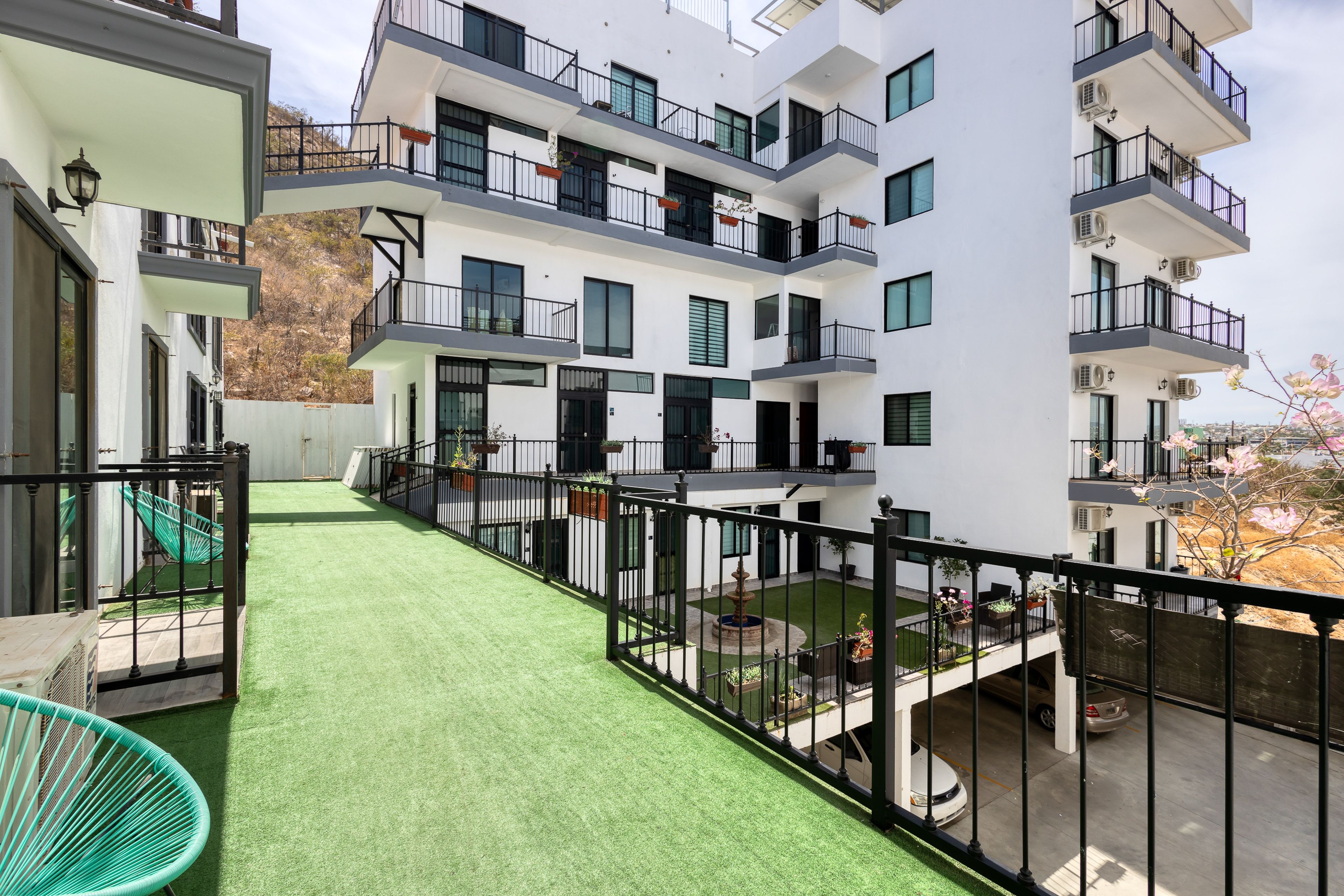A modern apartment building with multiple balconies, a green artificial lawn, and a view of the surrounding area.
