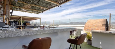 An outdoor bar area with a stone counter, two brown bar stools, and a view of distant mountains.