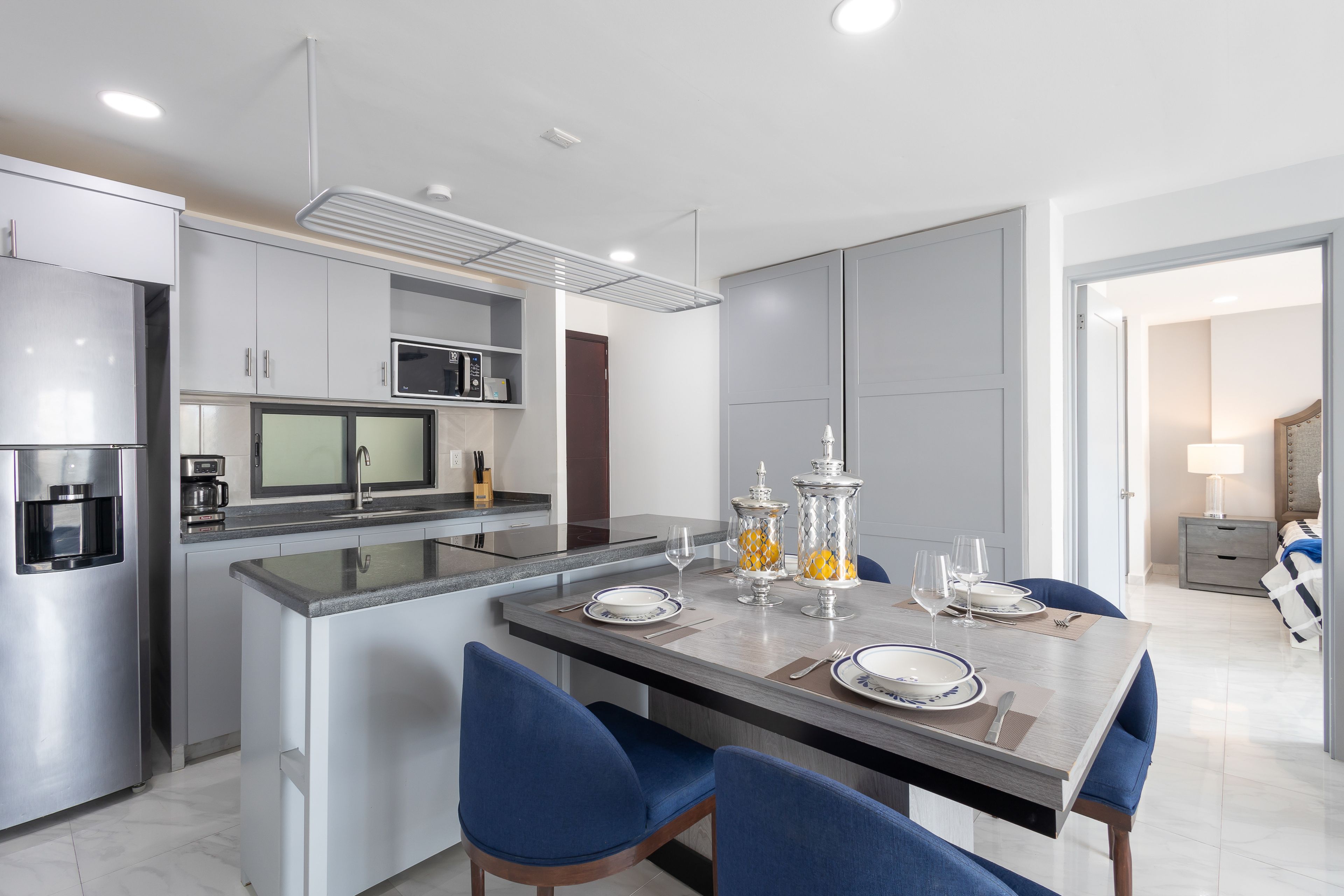 A modern kitchen with a central island, stainless steel appliances, and a dining area with blue chairs and a table set for two.