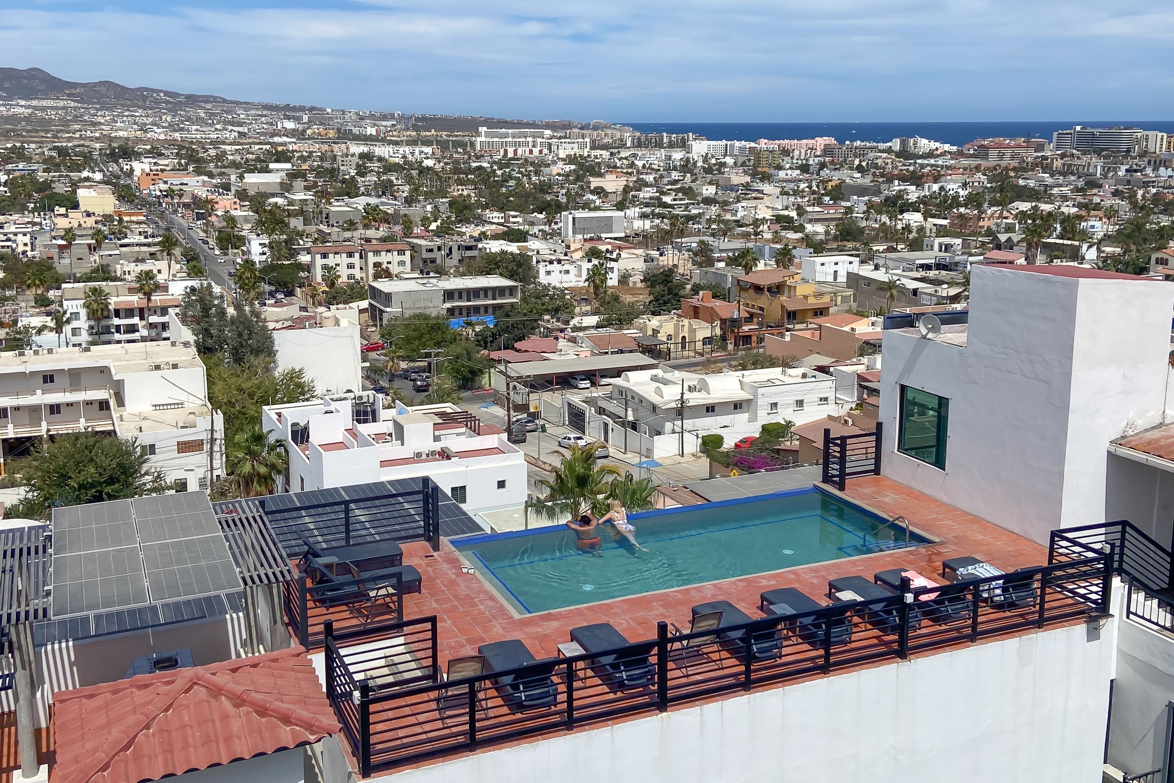 Una piscina en la azotea con tumbonas y vistas a una ciudad costera.