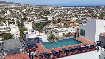 Una piscina en la azotea con tumbonas y vistas a una ciudad costera.