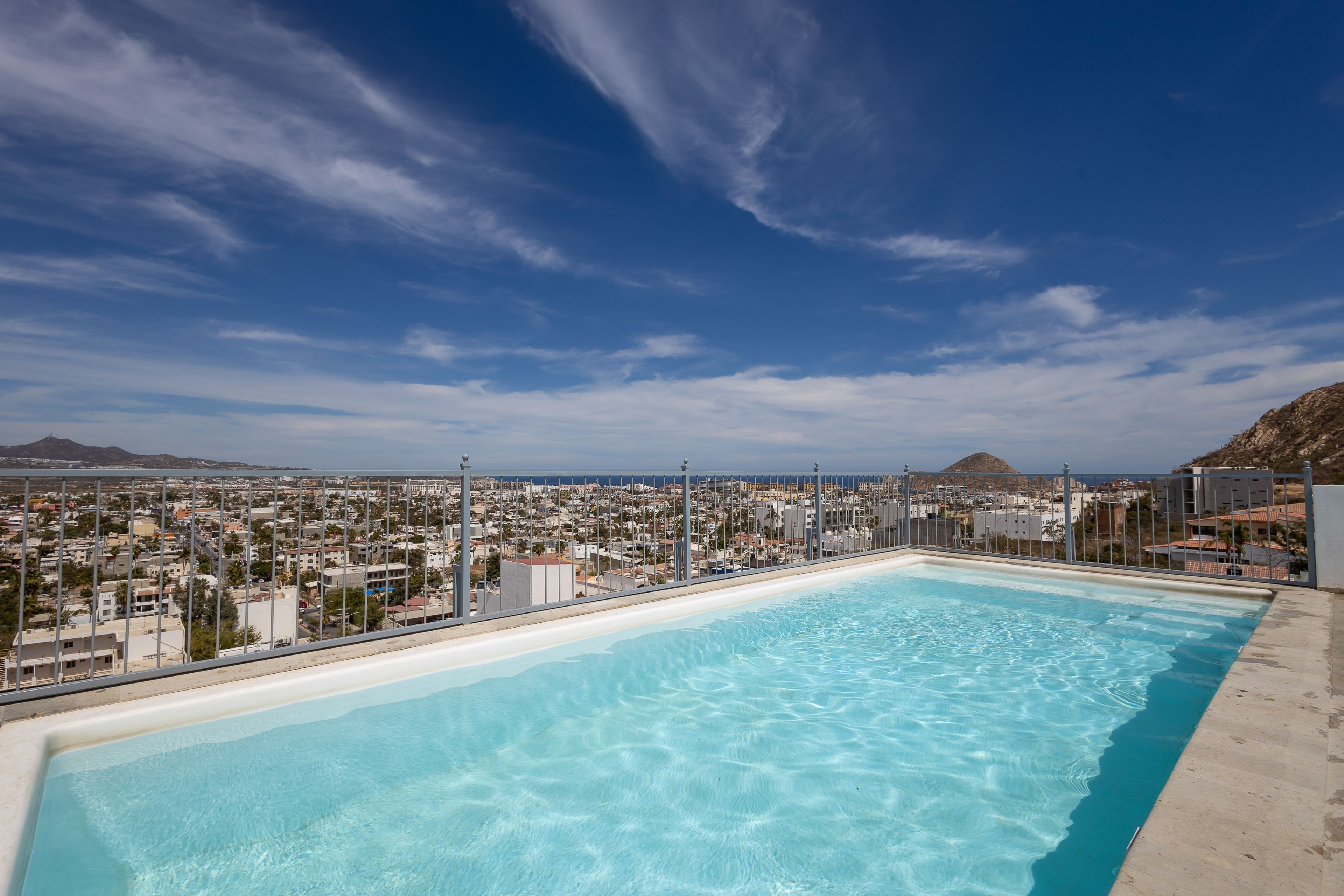 A rooftop swimming pool with a cityscape view, surrounded by a metal fence.