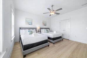 A hotel room with two beds, a ceiling fan, artwork on the walls, and a white door. - Sandy Cheeks | Pet-Friendly + Pool + Putting Green (Orange Beach)