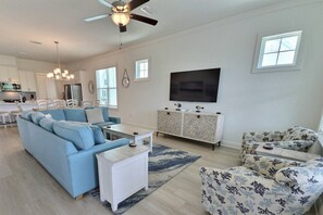 A modern living room with a sectional sofa, a white coffee table, a patterned armchair, a TV on a cabinet, and a ceiling fan. - Sandy Cheeks | Pet-Friendly + Pool + Putting Green (Orange Beach)