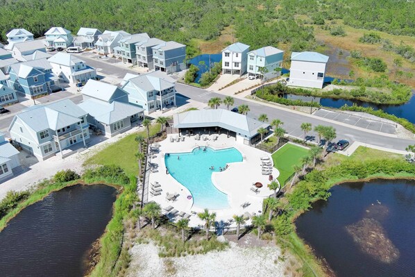A resort with multiple blue-roofed buildings, a central pool area with lounge chairs, and a surrounding natural landscape. - Sandy Cheeks | Pet-Friendly + Pool + Putting Green (Orange Beach)